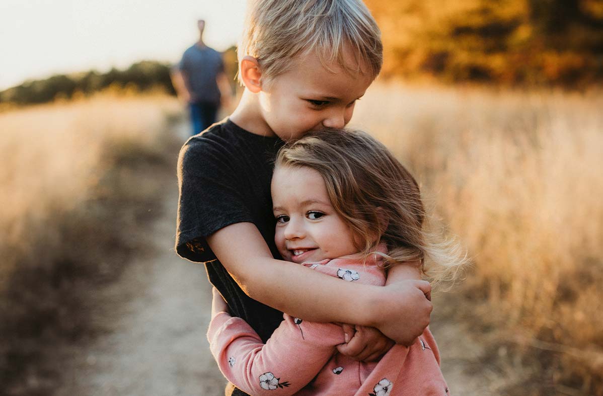 little kids hugging each other with parent walking behind